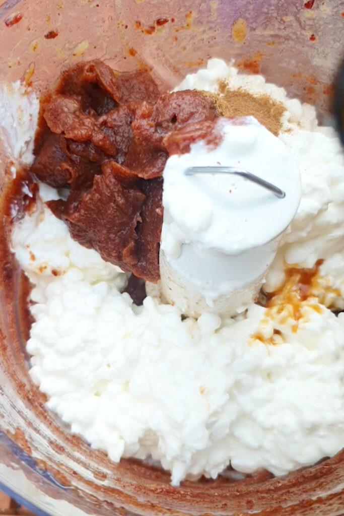 Cottage cheese, spices, and date paste in a food processor, ready to be blended into a creamy cottage cheese dip.