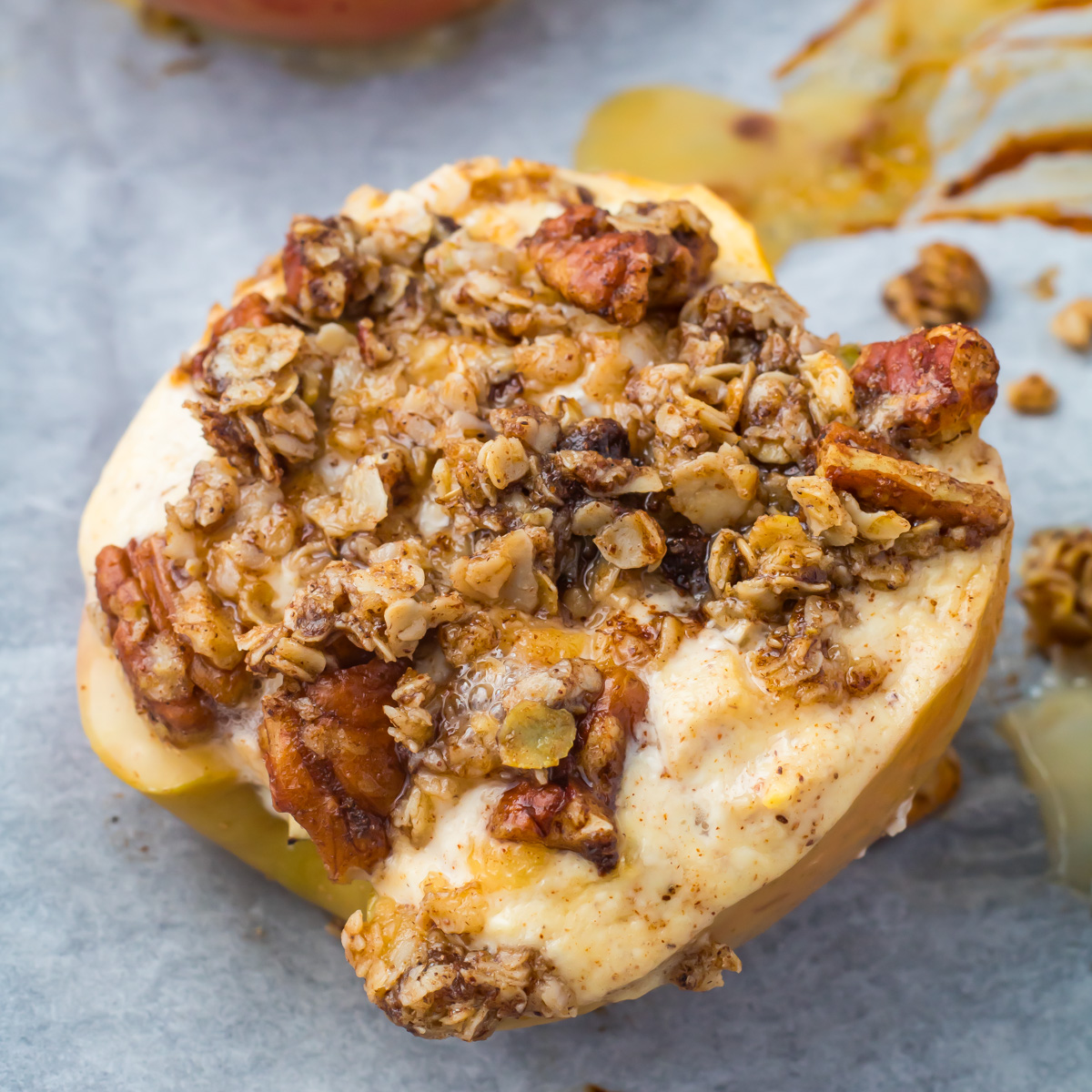 Cottoge Cheese baked apple half topped with a mixture of oats, nuts, and spices, sitting on a parchment-lined baking sheet.