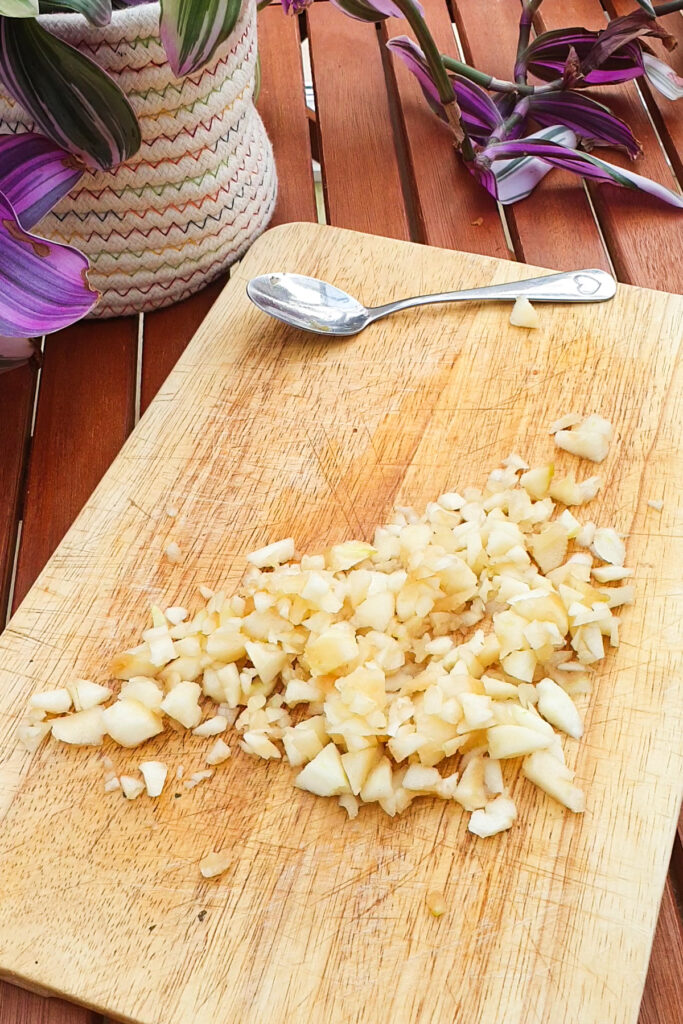Chopped pears on a wooden cutting board, with a spoon and a potted plant in the background on a wooden table—perfect for adding to your favorite cottage cheese recipes.