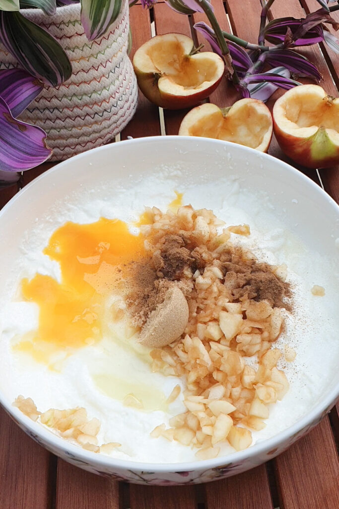 Large bowl of eggs, brown sugar, cinnamon, chopped apples, and cottage cheese on a wooden table.