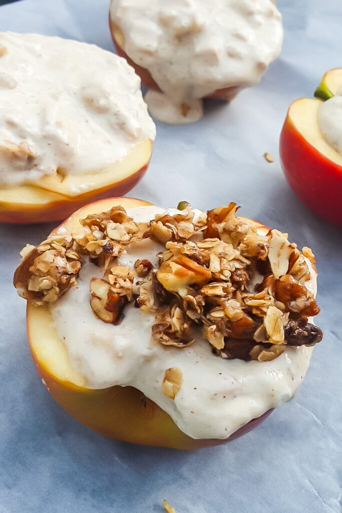 Half of an apple topped with creamy cottage cheese and crumble sits on parchment paper, with more similarly prepared baked apples in the background.