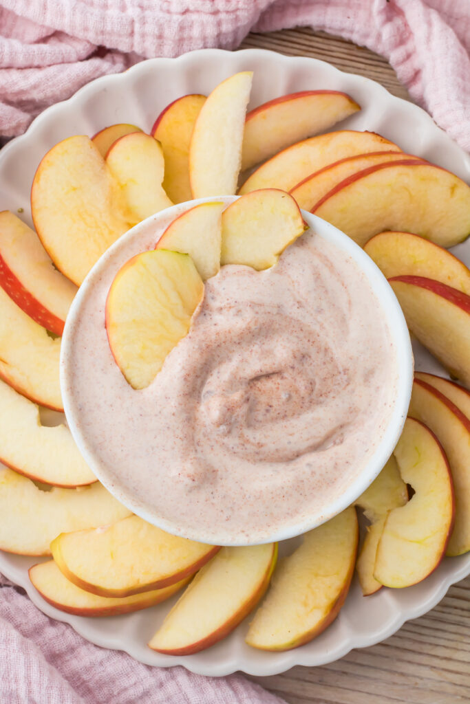 Sliced apples arranged on a round plate with a bowl of creamy cottage cheese apple dip in the center.