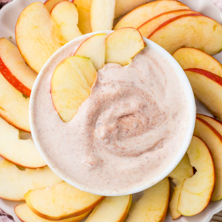 Sliced apples arranged around a bowl of creamy cottage cheese apple dip with cinnamon.
