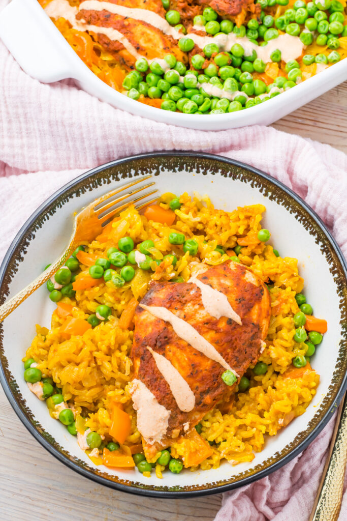 Peri peri chicken and rice featuring a seasoned chicken breast drizzled with sauce served over yellow rice with green peas.